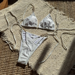 Close-up of white bikini set with pearl bead accents on textured woven background