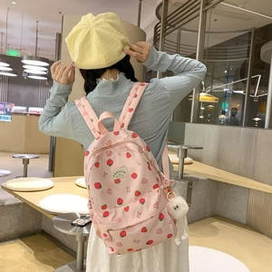 Pink strawberry school backpack with plush ball worn by a model in a cozy cafe