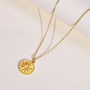 Detail of golden round pendant featuring a delicate sunburst engraving on a fine chain