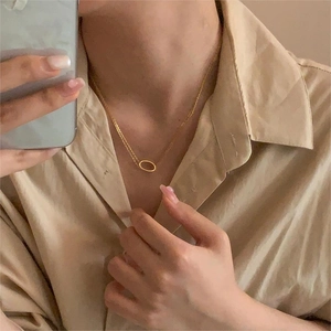 Detail of a minimalist gold oval pendant necklace worn on a khaki shirt collar