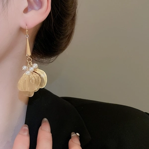 Detail of golden hollow petal earrings with pearls worn by a model in black attire
