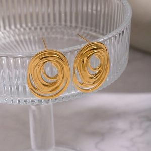 Close-up of gold geometric multilayer oval earrings on a glass stand over marble
