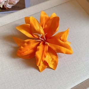 Close-up of vibrant orange Lycoris hair clip with satin petals on a beige tray