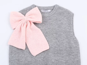 Detail of grey knitted vest featuring a large decorative pink bow and neck label