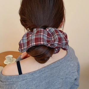 Detail of red and grey plaid oversized scrunchie on a bun hairstyle with soft fabric folds