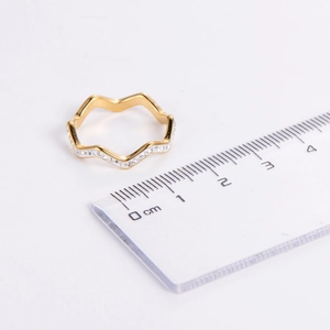 Detailed close-up of golden wavy ring with white zircons next to a measuring scale
