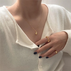 Close-up of golden organic balloon pendant necklace and matching rings on model