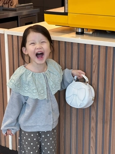 Close-up of a white round children's handbag with a large bow and elegant lace collar detail