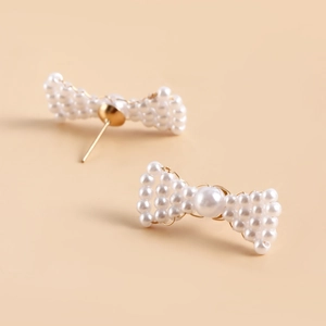 Detailed view of handmade bow-shaped earrings featuring white pearls and golden wire