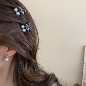Detailed view of silver bow pearl hair clips and orb earring set worn by a model
