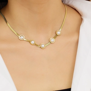 Detail of gold snake chain necklace with five bezel-set pearls on a white shirt collar