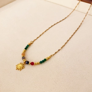 Détail du collier doré avec des perles colorées et un pendentif soleil poli brillant