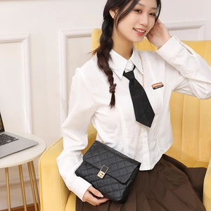 Elegant black quilted crossbody bag with gold chain strap shown on a model sitting on a sofa