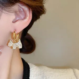 Gold-plated terrier puppy earrings with sparkling zircons worn by a model in warm light