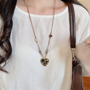 Detailed view of leopard print heart pendant necklace with beaded cord on linen fabric