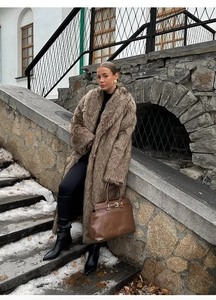 Detail of long brown faux fur coat and matching handbag against a snowy street background