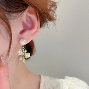 Gros plan sur des boucles d'oreilles muguet avec feuilles vertes et perles blanches