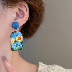 Detailed macro shot of French oil painting sunflower earrings on ear for size reference