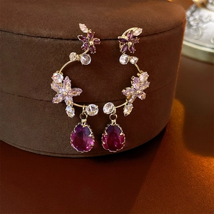 Elegant gold flower earrings with purple crystal teardrop pendants on brown velvet