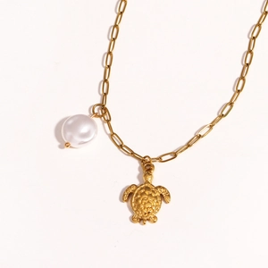 Detailed close-up of golden sea turtle pendant and white pearl on titanium necklace