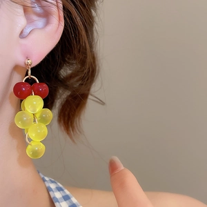 Macro shot of resin grape-shaped tassel drop earrings worn by a model in soft light