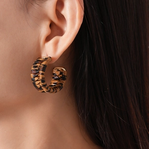 Close-up of leopard pattern woven C-shaped earrings worn by a model in a retro style