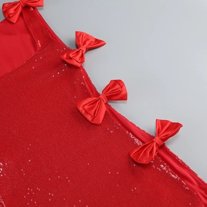 Detail of red sequin party dress featuring satin bow accents and shimmering texture