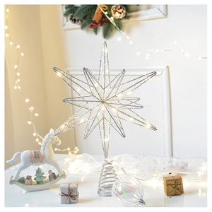 Detail of silver iron star Christmas tree topper with warm white LED lights in festive setting