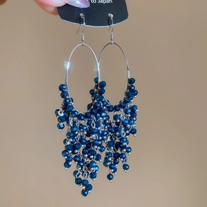 Detailed view of silver hoop earrings featuring dark blue faceted bead tassels being held