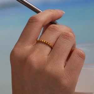 Minimalist gold gear patterned stainless steel ring worn on model hand by the beach