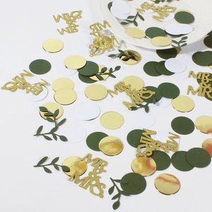 Close-up of gold MR & MRS sequins with green leaves and round paper party confetti