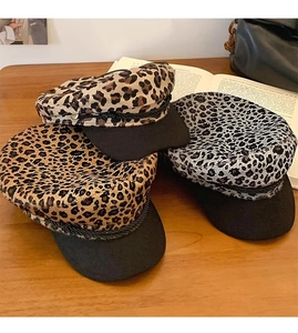 Detail of stacked leopard print newsboy hats in khaki and grey on a rustic wooden table