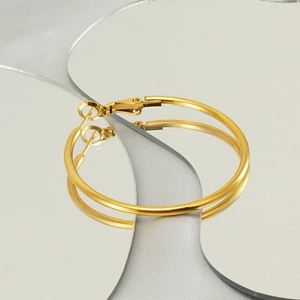 Detailed view of large gold stainless steel hoop earrings on a reflective mirror surface