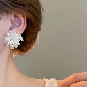 Close-up of elegant white floral stud earrings with pearl details on model ear