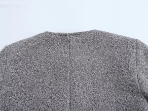 Détail du col d'une veste en tweed gris montrant la texture tissée sur fond blanc