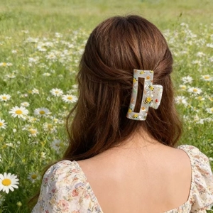 Dettaglio del mollettone rettangolare con api e fiori indossato su capelli castani
