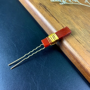 Detail of red crystal agate hair pin with gold wire wrapping on a wooden tray