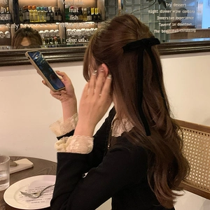 Elegant black velvet ribbon bow hair clip shown on model in a stylish bistro setting