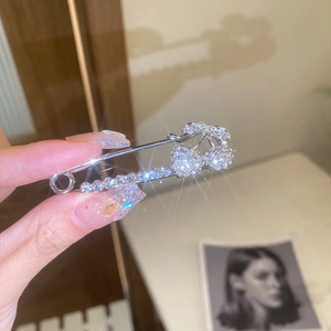 Macro view of crystal encrusted silver safety pin brooch with tassel and pearls