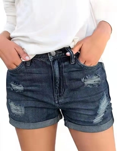 Detailed macro view of distressed denim texture and frayed hem on dark blue jean shorts