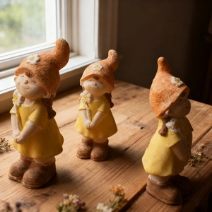 Trois figurines de fées en robes jaunes et chapeaux orange sur une table en bois