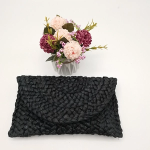 Dettaglio di una pochette a busta nera in paglia intrecciata a mano con trama fitta