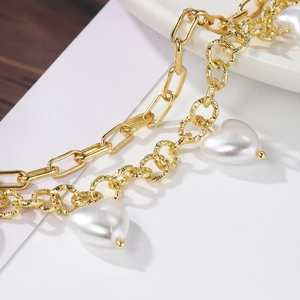 Macro shot of gold double-layer chain bracelet with elegant white heart pearl charms