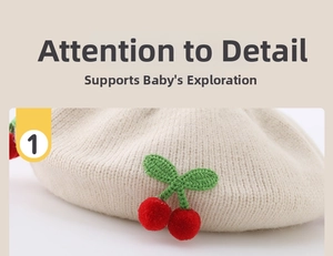 Close-up of beige knit baby beret featuring handcrafted red cherry and green leaf details