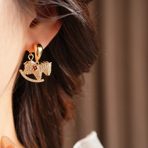 Close-up of a gold rocking horse earring with crystals and a red gem worn by a model