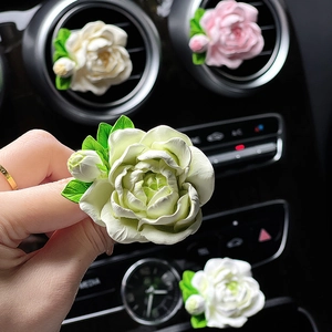 White jasmine flower car vent clip diffuser with green leaves on dashboard