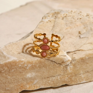 Detailaufnahme eines goldfarbenen Rings mit rosa Edelsteinen auf Natursteingrund
