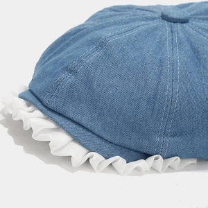 Close-up of blue denim newsboy hat featuring white chiffon ruffled edges and fine stitching
