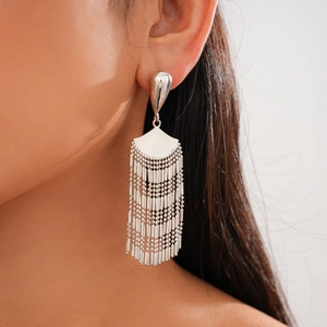 Close-up of silver fan-shaped fringe earrings with metallic tassels worn by a model