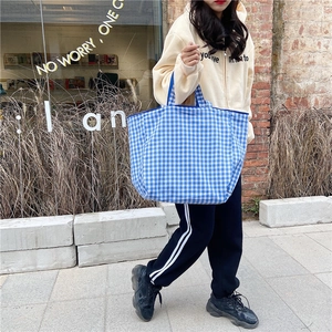 Detailed view of blue and white checkered canvas tote bag worn by model outdoors